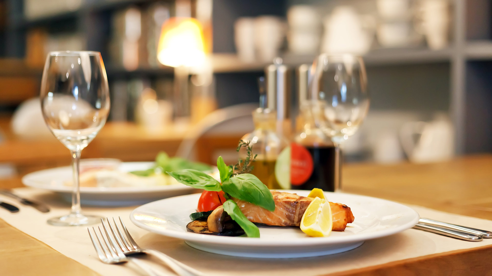 Ein stilvoll gedeckter Restauranttisch mit Gourmetgericht, leeren Weingläsern und stimmungsvoller Beleuchtung.