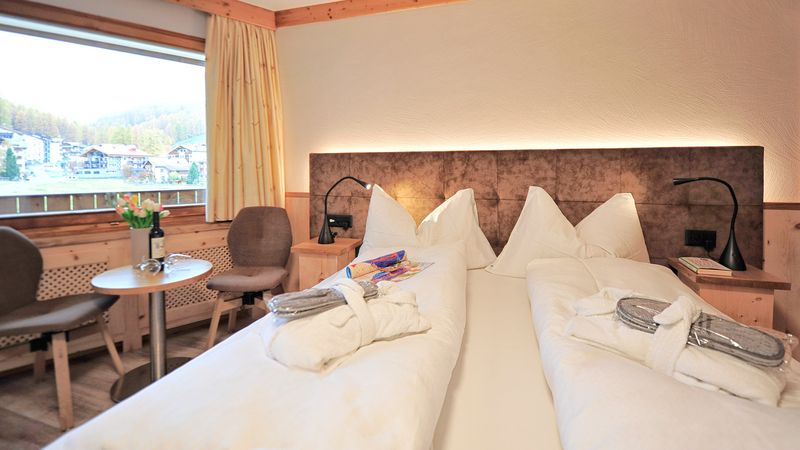 Gemütliches Hotelzimmer mit Doppelbett und Holzmöbeln, Aussicht auf grüne Hänge